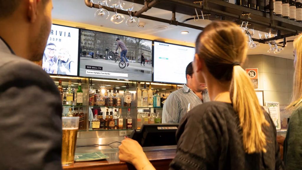 People at a bar looking at a digital screen displaying Red Bull video content.